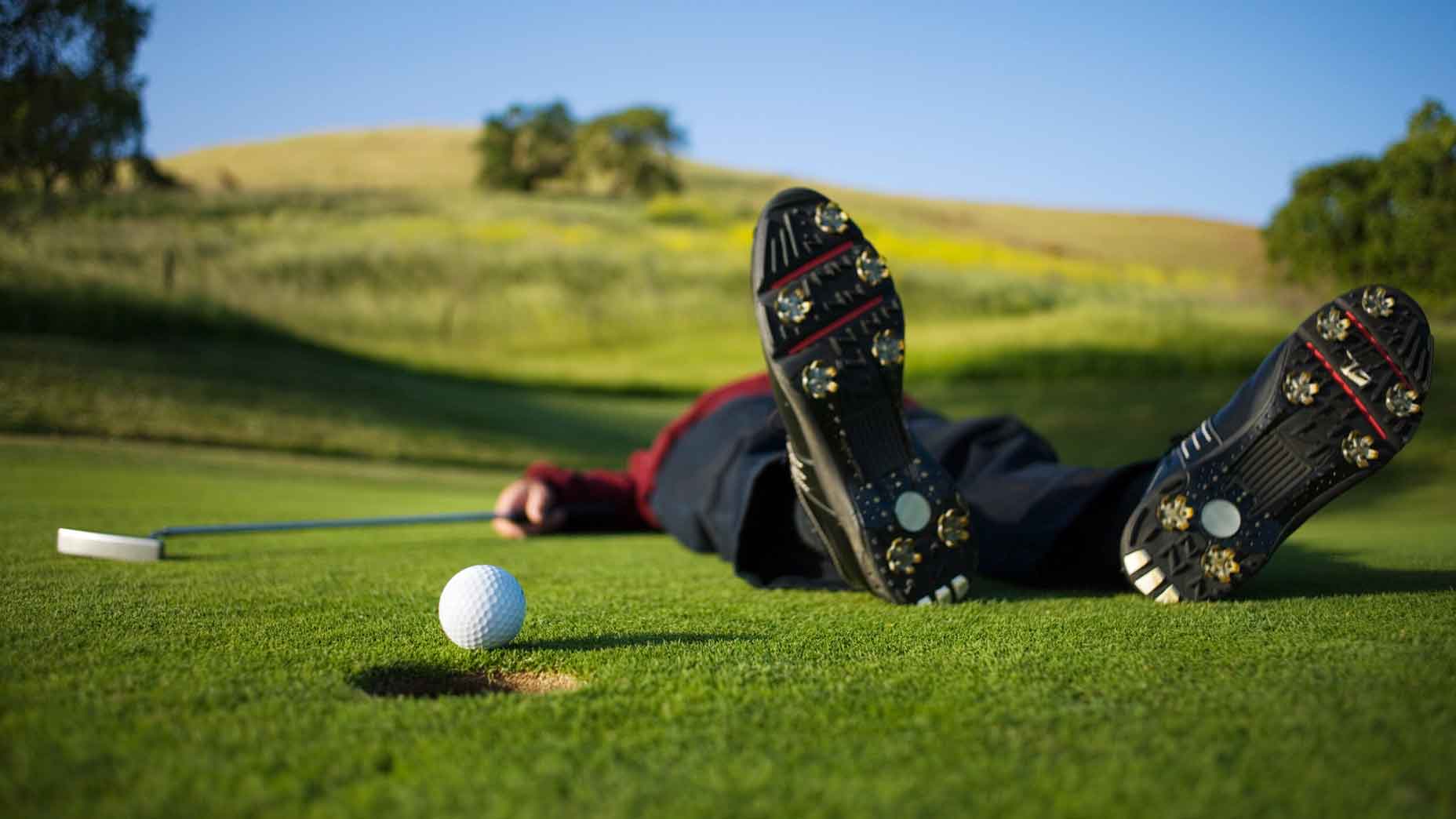 Golfer lying on green, ball on edge of hole