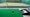 golfer sets up club behind ball on green mat with range balls next to it